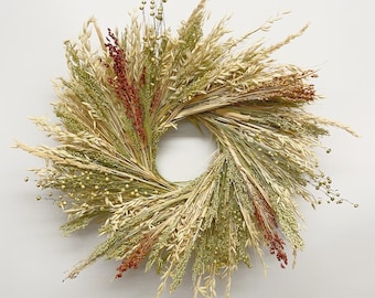 May include: A circular wreath composed of dried grasses and grains in shades of beige, green, and red. The wreath is arranged in a radial pattern, with the stems of the grasses forming the base and the seed heads extending outwards.