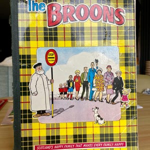 May include: A vintage copy of "The Broons" comic book. The cover is yellow and black tartan, with the title in red and blue. A cartoon illustration of a family is featured, along with the text "Scotland's Happy Family That Makes Every Family Happy."