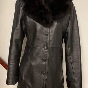 May include: A black leather coat with a black fur collar. The coat has a button closure and a fitted silhouette.