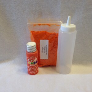 Op de afbeelding: Een doorzichtige plastic knijpfles met een witte dop, een klein flesje oranje acrylverf en een zakje met oranje flock. Op het zakje staat "Orange flocking" gedrukt.