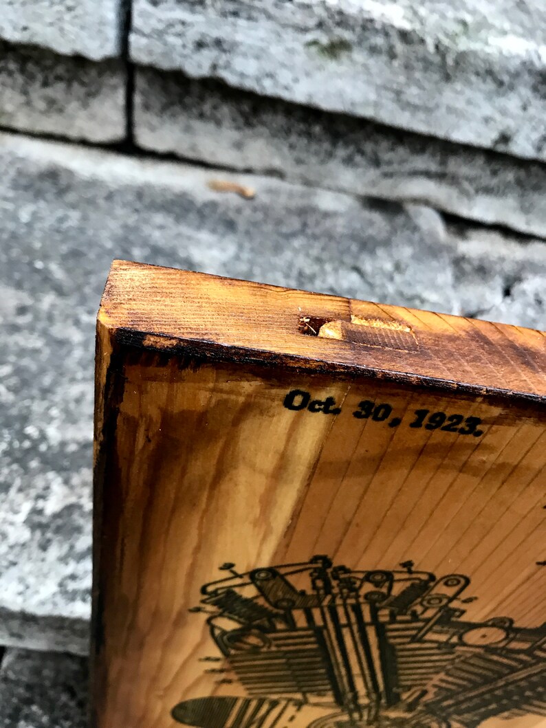 Puede incluir: Un letrero de madera con una ilustraci&oacute;n en blanco y negro de un motor de motocicleta. La fecha "Oct. 30, 1923" est&aacute; impresa en el letrero.