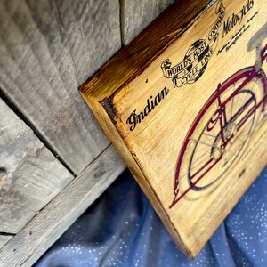 May include: A vintage wooden sign with a black and white illustration of an Indian motorcycle. The sign reads "Indian, World's Most Complete Cycle Line, Motorcycles".