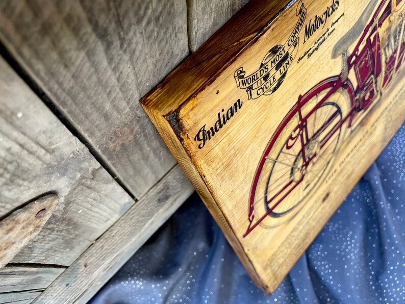 May include: A vintage wooden sign with a black and white illustration of an Indian motorcycle. The sign reads "Indian, World's Most Complete Cycle Line, Motorcycles".