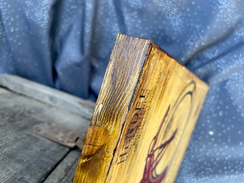 May include: A wooden sign with a vintage design featuring the text "Heindee" and a stylized illustration of a bicycle. The sign has a dark brown stain and a distressed look.