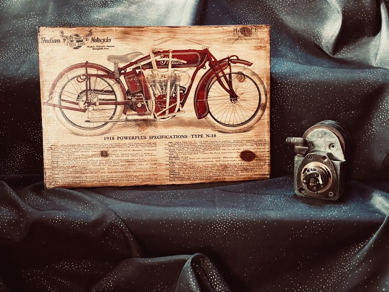 May include: A vintage wooden sign with a black and white illustration of a red 1918 Indian Motorcycle. The sign has the text "Indian Motorcycles" and "1918 Powerplus Specifications - Type N-18" printed on it.