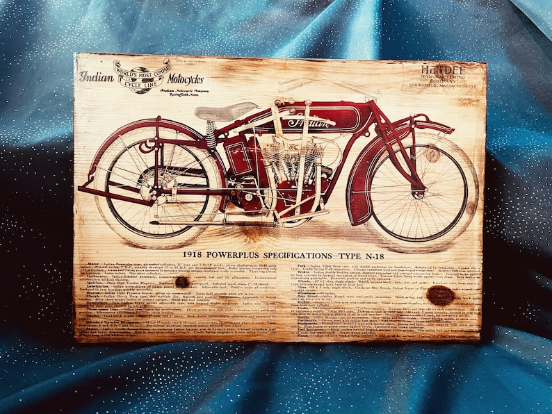 May include: A vintage advertisement for a 1918 Indian Powerplus motorcycle, model N-18. The ad features a detailed illustration of the motorcycle in red and black, with the words "Indian Motorcycles" and "World's Most Complete Cycle Line" at the top. The ad also includes a list of specifications for the motorcycle.