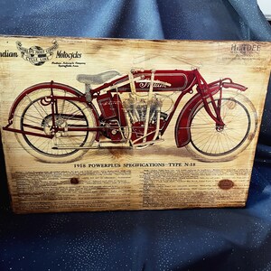 May include: A vintage advertisement for an Indian motorcycle, featuring a red motorcycle with a black engine and white wheels. The text on the advertisement reads "Indian World's Most Copied Cycle Line Motorcycles" and "1918 Powerplus Specifications - Type N-18".