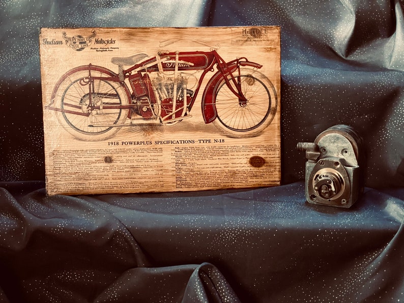 May include: A vintage wood plaque with a red and black illustration of a 1918 Indian Motorcycle, model N-18. The plaque features the text "Indian Motorcycles" and "1918 Powerplus Specifications - Type N-18".