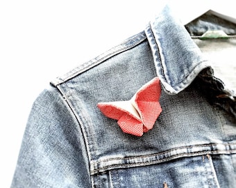 May include: A red origami butterfly pinned to the collar of a blue denim jacket.
