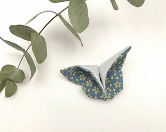 May include: A blue origami butterfly with a yellow floral pattern. The butterfly is folded from fabric and is sitting on a white surface.
