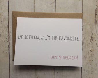 May include: A white card with black text that reads "We both know I'm the favourite. Happy Mother's Day!" The card is on a woodgrain background.