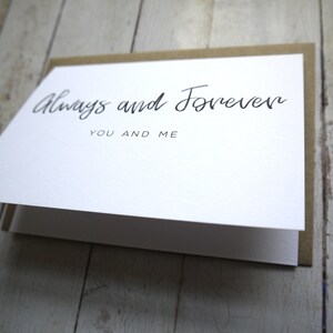 May include: A white card with brown paper backing. The card has black calligraphy that reads "Always and Forever" with the words "You and Me" underneath.
