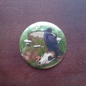 May include: A black crow perched on a white animal skull, surrounded by green foliage and red mushrooms. The crow is sitting on a tree stump with moss growing on it.