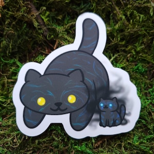 May include: A black and blue cat sticker with glowing yellow eyes. The cat is standing on its hind legs and has a smaller black and blue cat sticker behind it.