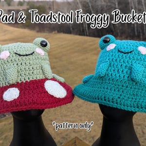 May include: Two crochet bucket hats labeled Lily Pad & Toadstool Froggy Bucket Hat and *pattern only*. One hat is light green with a red brim featuring white spots. The other is teal with a pink flower accent. Both feature frog eyes.