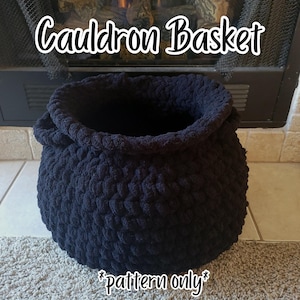 May include: A black, round, crocheted basket with a thick, textured yarn construction and a wide opening. The text "Cauldron Basket" is printed in white at the top, and the text "*pattern only*" is printed in white at the bottom of the image.