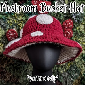 Könnte beinhalten: Ein gehäkelter Fischerhut in Dunkelrot mit weißen kreisförmigen Punkten, der einem Pilzhut nachempfunden ist. Der Text Mushroom Bucket Hat und *pattern only* sind sichtbar. Der Hut hat eine breite Krempe und eine strukturierte Garnverarbeitung.