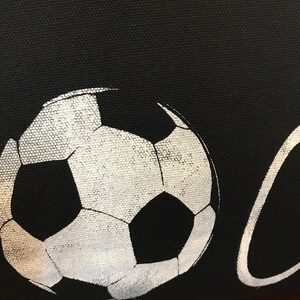 K&ouml;nnte beinhalten: Eine schwarze Stofftasche mit einem wei&szlig;en Fu&szlig;ball-Motiv und dem aufgedruckten Wort "Goal".