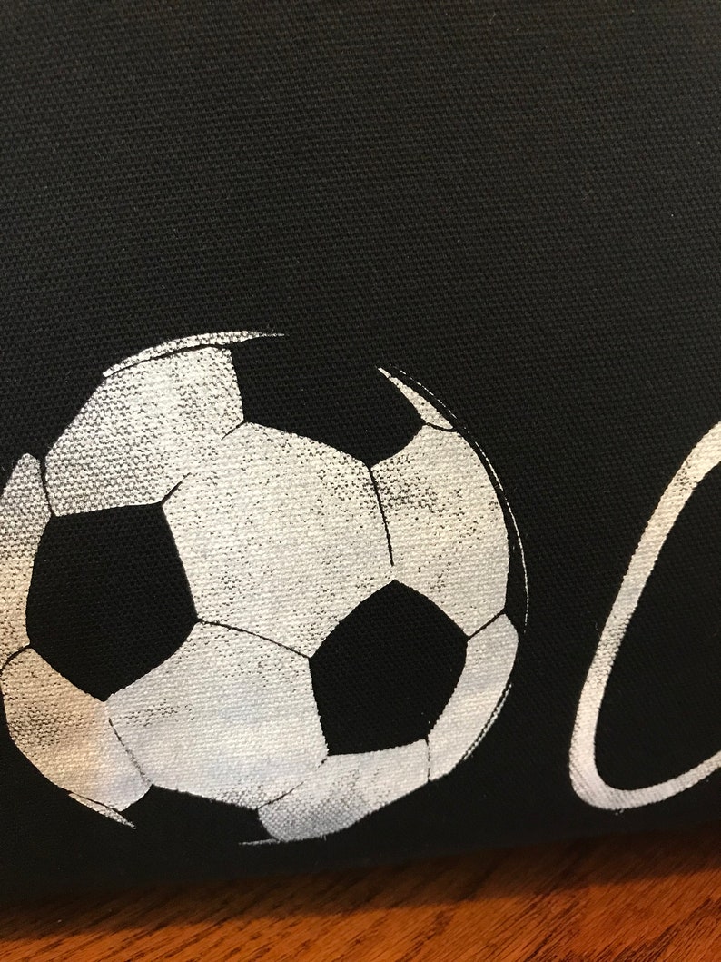 K&ouml;nnte beinhalten: Eine schwarze Stofftasche mit einem wei&szlig;en Fu&szlig;ball-Motiv und dem aufgedruckten Wort "Goal".