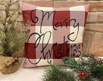 May include: Red and white plaid throw pillow with the text "Merry Christmas" in black cursive writing.