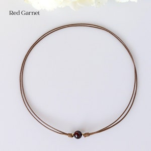 May include: A simple brown leather cord necklace with a single red garnet gemstone bead.