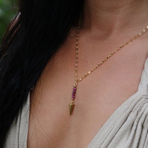 May include: A gold chain necklace with a small gold pendant shaped like a point. The pendant is adorned with small pink gemstones.