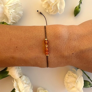 May include: A brown cord bracelet with a row of six small, orange carnelian beads and gold spacers.