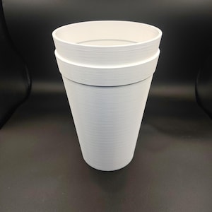Puede incluir: Un vaso blanco, cónico y cilíndrico, con una superficie texturizada y un borde horizontal distintivo cerca de la parte superior. El vaso presenta un interior liso y una abertura ancha, mostrando un diseño simple y funcional con acabado mate.