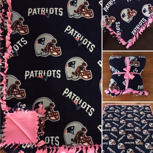May include: A navy blue fleece blanket with a pink knotted fringe. The blanket features a repeated pattern of a football helmet with the word "Patriots" printed on it.