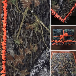 Op de afbeelding: Een camouflage fleece deken met een oranje geknoopte franje rand. De deken is gevouwen en in het midden vastgebonden met een lint.