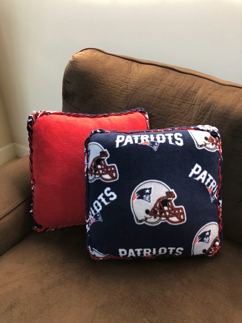 May include: Two decorative throw pillows, one red and one blue. The blue pillow has a repeated pattern of white football helmets and the word "Patriots" in red and white lettering.