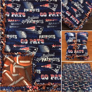 May include: A blue and brown fleece blanket with a New England Patriots theme. The blanket features the team logo, the words "Go Pats", and stars. The blanket is tied with brown ribbon.