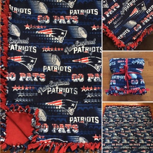May include: A blue and red fleece blanket with the New England Patriots logo and the words "Go Pats" repeated throughout. The blanket is tied with a red ribbon and has red fringe around the edges.