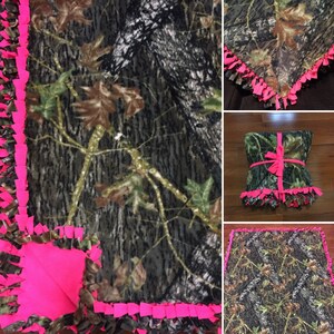 Op de afbeelding: Een camouflage fleece deken met roze franjes. De deken is gemaakt van zacht, comfortabel fleece en heeft een camouflagepatroon. De franjes zijn gemaakt van roze garen en voegen een vleugje whimsy toe aan de deken.