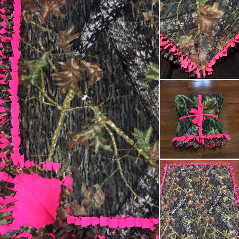 Op de afbeelding: Een camouflage fleece deken met roze franjes. De deken is gemaakt van zacht, comfortabel fleece en heeft een camouflagepatroon. De franjes zijn gemaakt van roze garen en voegen een vleugje whimsy toe aan de deken.