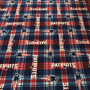 May include: A blue and red fleece blanket with a plaid pattern and the word "PATRIOTS" repeated throughout. The blanket has a knotted fringe border.