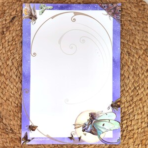 May include: A decorative stationery sheet with a purple watercolor border and illustrations of moths and a fairy riding a moth. The design includes a crescent moon and swirling lines. The stationery is on a woven surface.