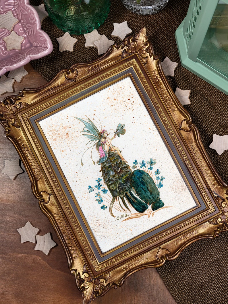 May include: A framed illustration of a fairy with green wings and a pink dress sitting on a bed of green leaves. The fairy is holding a green four-leaf clover. The background is a light brown with white speckles.