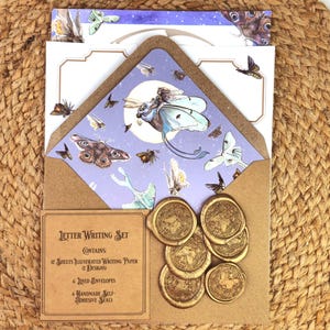 May include: A letter writing set featuring illustrated paper and envelopes with a moth and butterfly theme. The set includes six gold-colored wax seals. The set is displayed on a woven, tan surface.