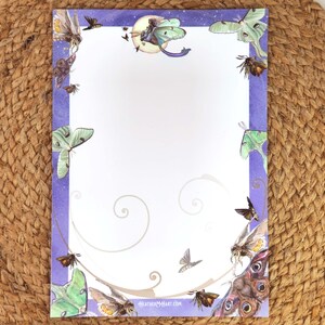 May include: A sheet of stationery with a purple border featuring illustrations of moths and butterflies. The design includes a crescent moon and stars at the top, with the text "heatherMcArt.com" at the bottom. The stationery is on a woven mat.