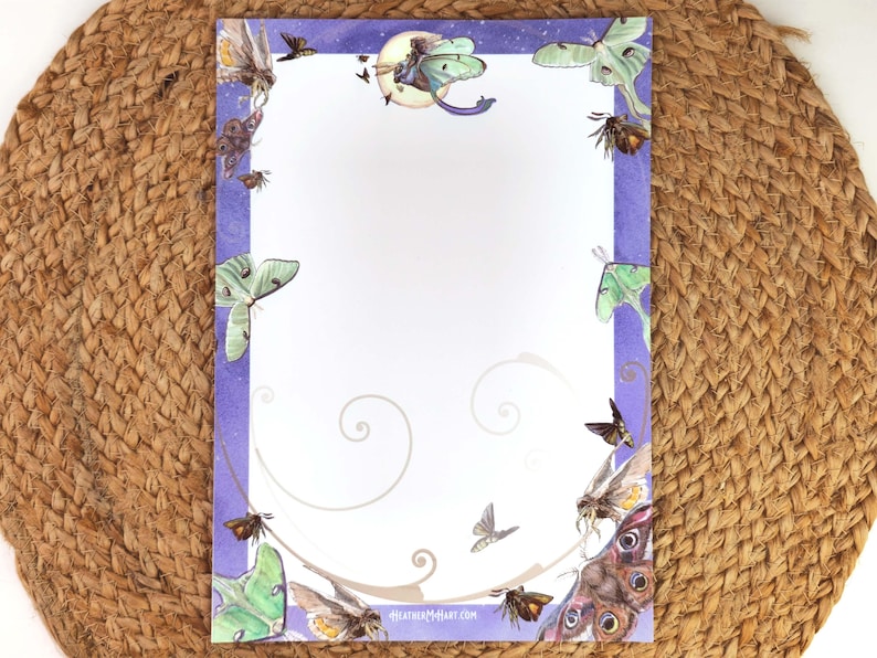 May include: A sheet of stationery with a purple border featuring illustrations of moths and butterflies. The design includes a crescent moon and stars at the top, with the text "heatherMcArt.com" at the bottom. The stationery is on a woven mat.