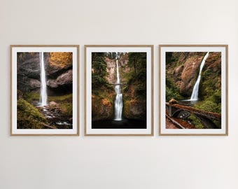 May include: A set of three framed prints depicting a waterfall cascading down a rocky cliffside. The prints are in a natural wood frame and feature a muted colour palette of greens, browns, and greys.