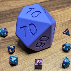 May include: A large, blue, multi-sided die with the number 70 visible, surrounded by smaller, multi-coloured dice. The dice are arranged on a wooden surface, showcasing a tabletop gaming theme.