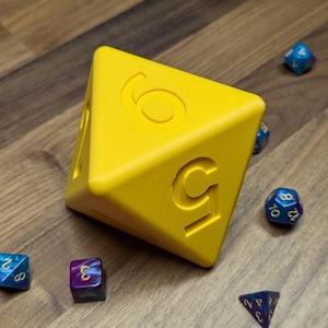 May include: A large yellow die displaying the number 5, with smaller multi-sided dice in blue, purple, and gold scattered around it. The dice are arranged on a wooden surface, creating a game-themed scene.