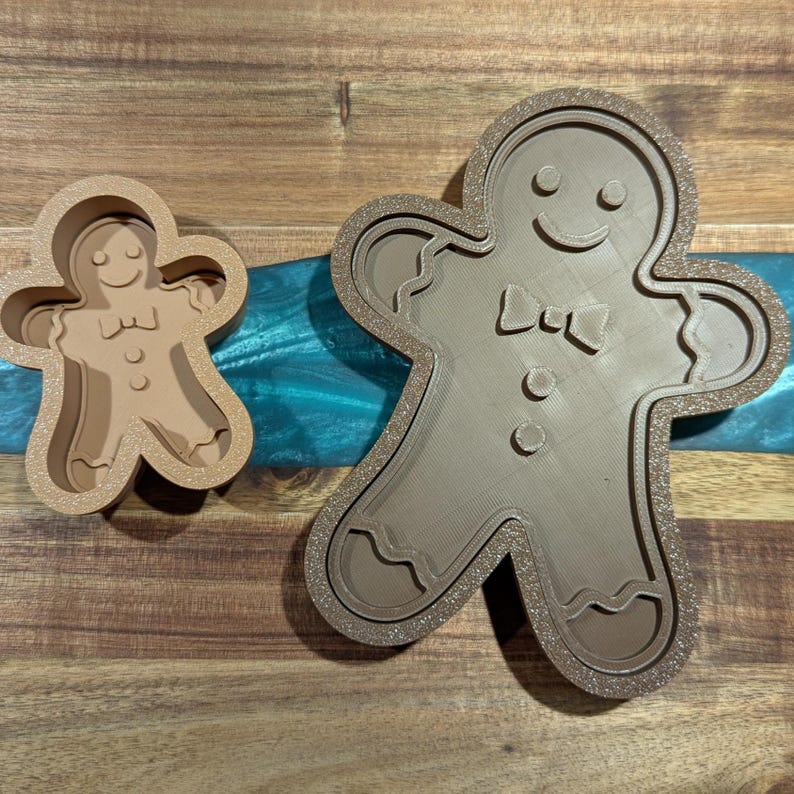 Puede incluir: Dos cortadores de galletas de hombre de jengibre marrones. Uno es una versi&oacute;n m&aacute;s peque&ntilde;a y s&oacute;lida, y el otro es un contorno m&aacute;s grande y detallado. Ambos tienen caras sonrientes, pajaritas y detalles de botones.