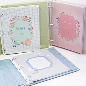 May include: Three baby memory books with floral designs. The covers are light blue, pink, and green with white checkered patterns. Each cover has a floral wreath with a blank space for the baby's name and birth date.