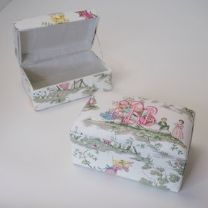 May include: Two white rectangular boxes with a floral pattern and a pink embroidered monogram. The box on the left is open and the box on the right is closed.