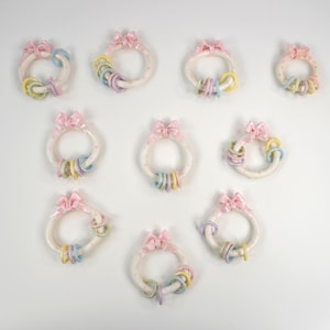 Puede incluir: Diez coronas de cerámica de color pastel con lazos rosas y anillos de color pastel. Las coronas están decoradas con pequeños lunares blancos.