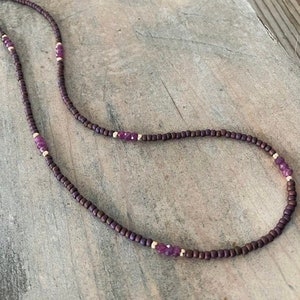 May include: A delicate necklace with small brown beads and purple gemstone accents.