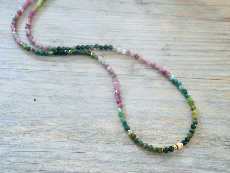 May include: A multi-colored gemstone necklace with a gradient of pink, blue, and green beads. The necklace is made with small, faceted beads and has a gold clasp.